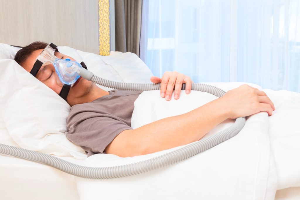 A man with sleep apnea sleeping peacefully in bed while wearing a CPAP nasal mask.
