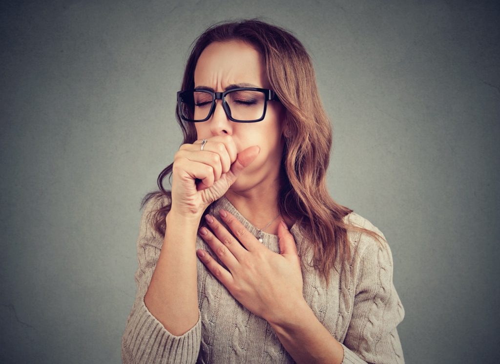 A woman holding her hand to her throat while coughing in discomfort.