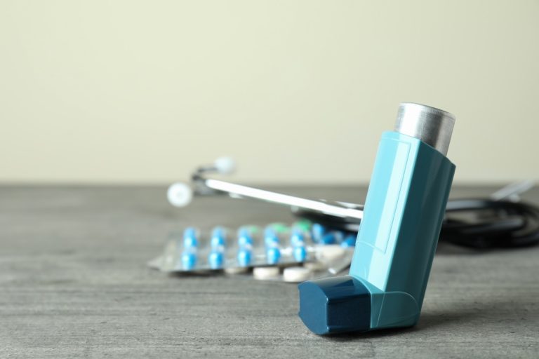 An asthma inhaler resting on a table alongside a peak flow meter and medical accessories.
